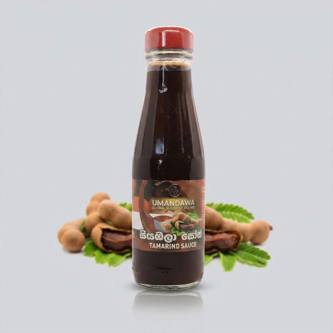 Glass bottle of tamarind sauce with red cap, tamarind pods and leaves in background
